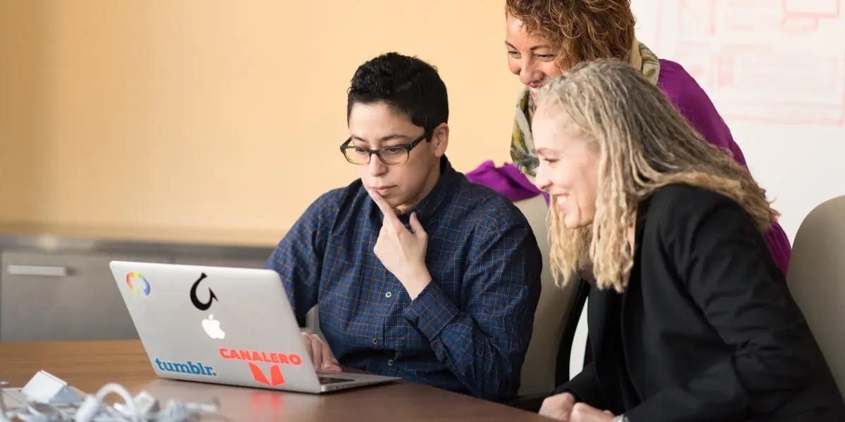 Three Ruby on Rails developers sit looking at code on a laptop in a startup office.