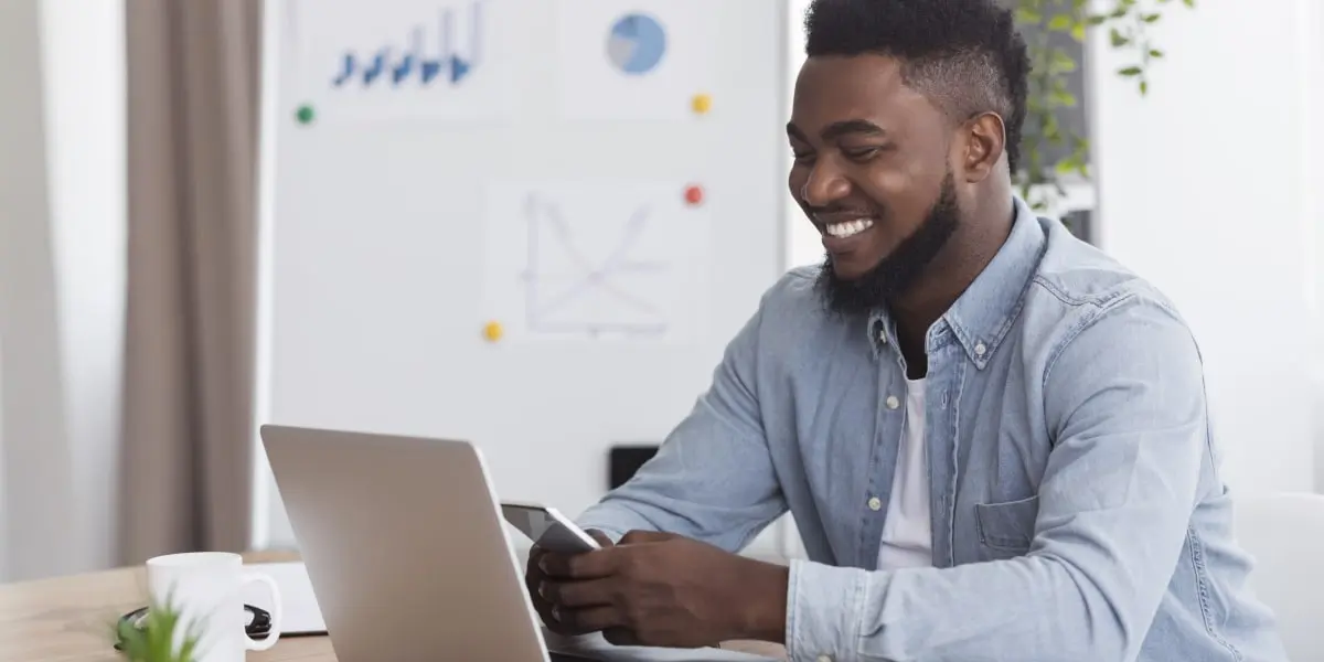 A social media specialist smiling looking at a phone, with a laptop in view