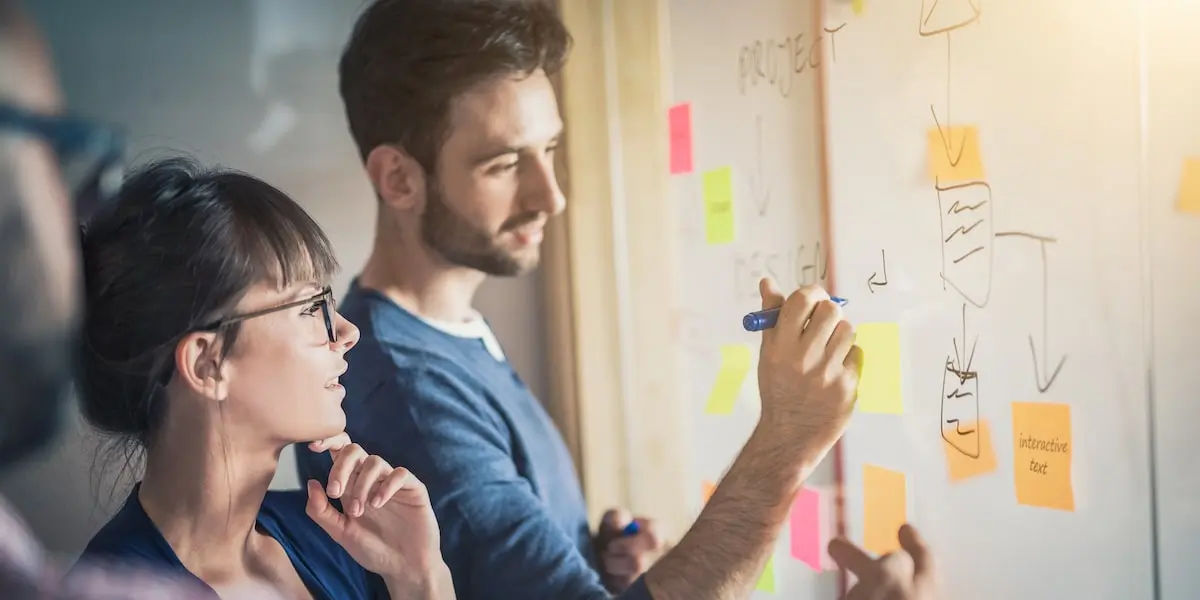 UX designers using UX best practices to workshop a design at a whiteboard with sticky notes on