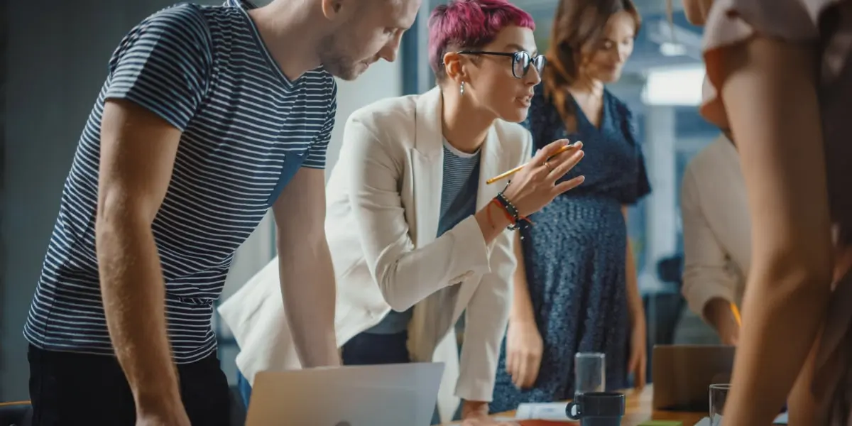 Web developers standing in a meeting around a laptop in a startup, discussing which approach to take.