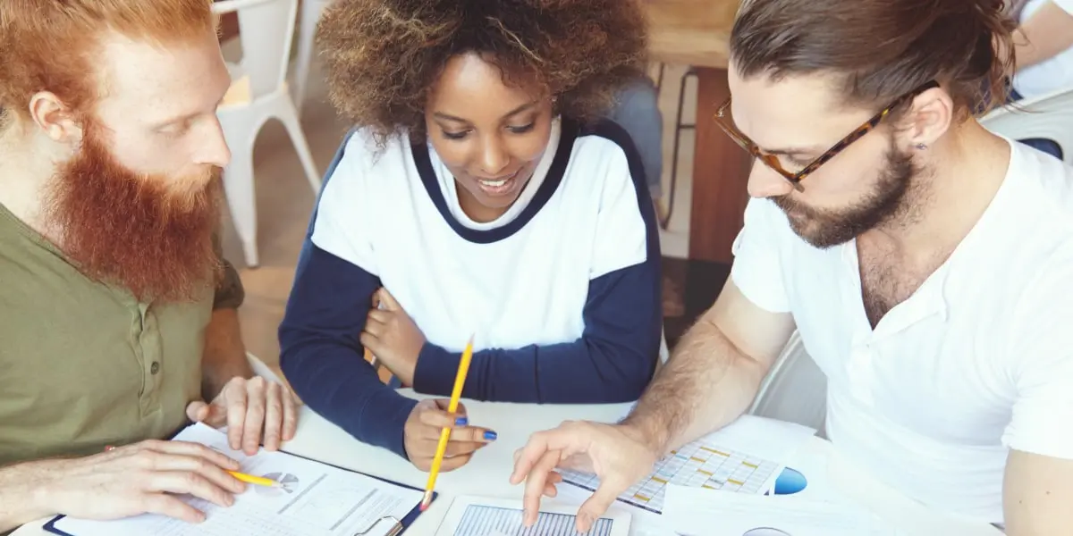 A digital marketing specialist sitting with two colleagues at a desk, looking at graphs and charts