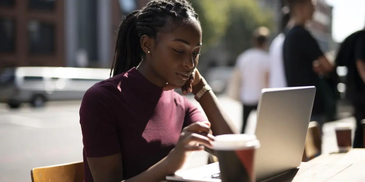 A social media specialist sitting at a table in the sunshine, looking at a laptop