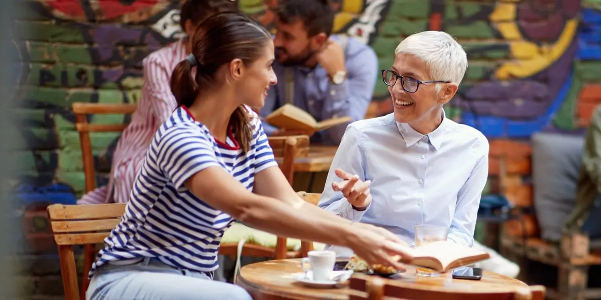 Two friends sitting at a cafe table outside, discussing whether digital marketing bootcamps are worth it