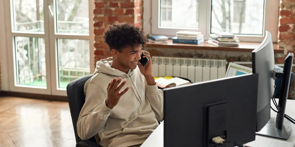 A digital marketing professional sitting at a desk, speaking into a telephone, looking at marketing portfolio examples on a desktop computer