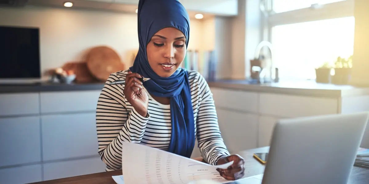 A social media specialist sitting in a kitchen, looking at documents and a laptop