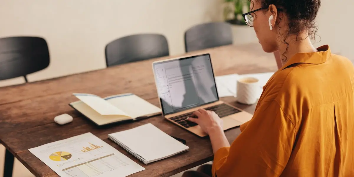 A freelance digital marketer sits at her desk with her laptop. She has a print out of a marketing analysis.