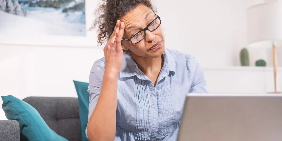 An aspiring digital marketer sitting on a sofa with a laptop, weighing up whether to do a digital marketing degree or a digital marketing bootcamp