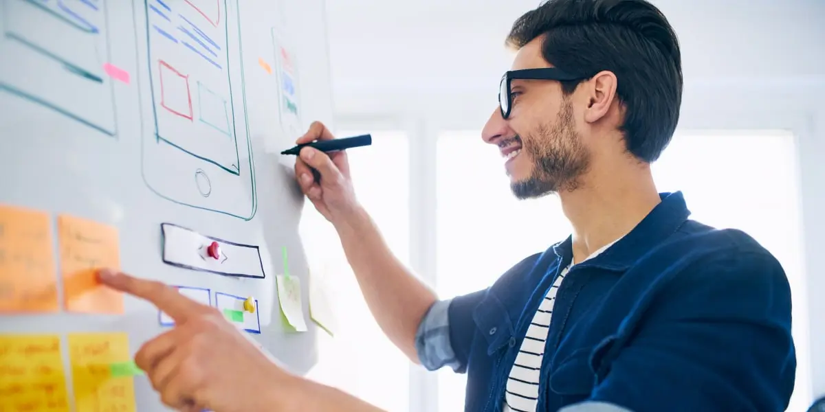 A UX designer standing at a whiteboard covered in sticky notes and sketches