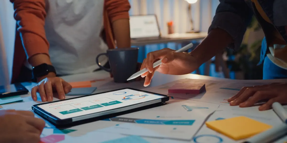 Two designers working at a table in a darkened room, looking at screens on a table covered in sticky notes and project reports, contemplating design careers.