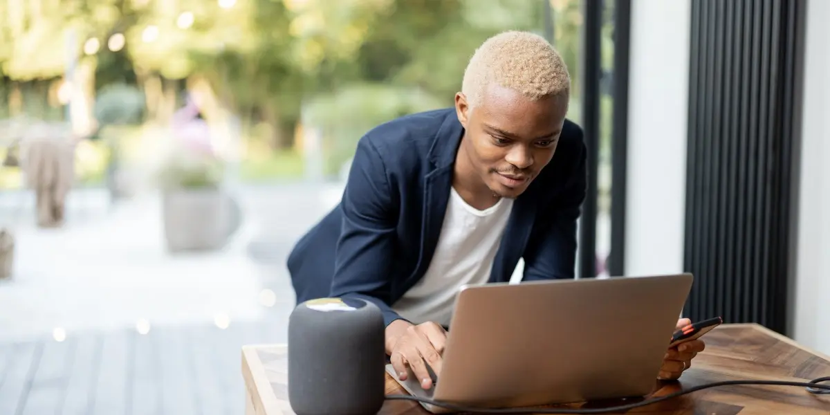 A man stands at a kitchen table working at a laptop taking free coding classes.