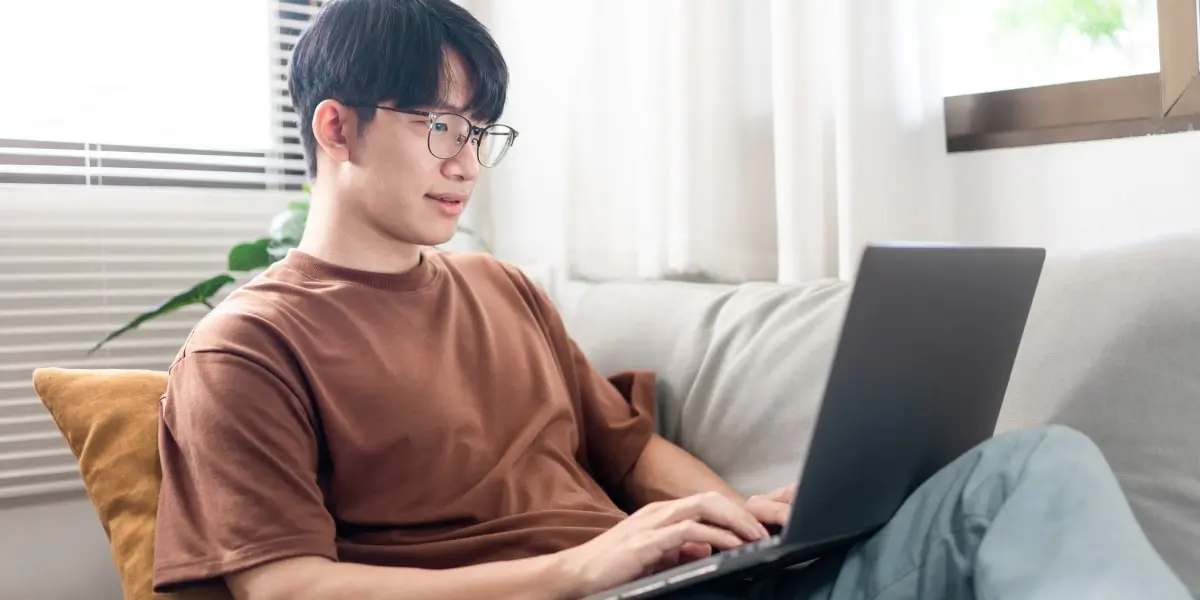 A designer sits on his couch, working on a laptop on the sofa.