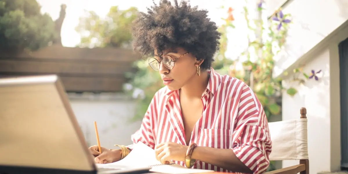 A woman sits in her garden with her laptop and notepad teaching herself UX design.