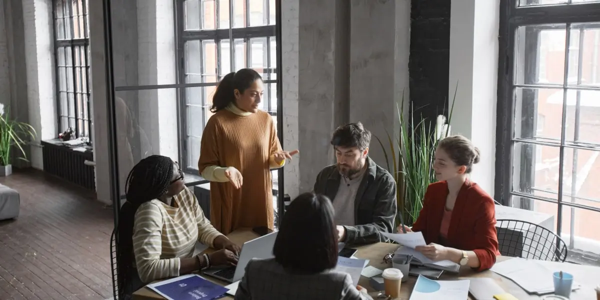 A product manager and a product owner sit with their colleagues in a meeting in a startup office.