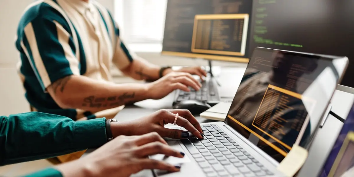 Two coders sit in an office typing lines of code at their computers.