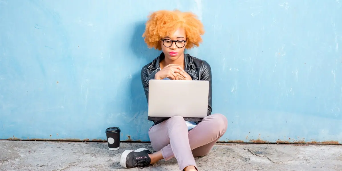 A woman sits on the ground with her laptop writing a UX cover letter.