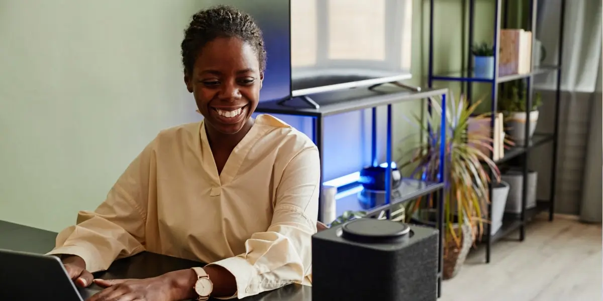 A UI designer in a wheelchair works at a laptop with a smart speaker.