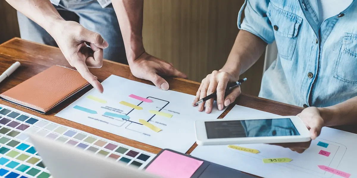 Two UX designers at a desk applying visual hierarchy to a mobile app screen resdesign.