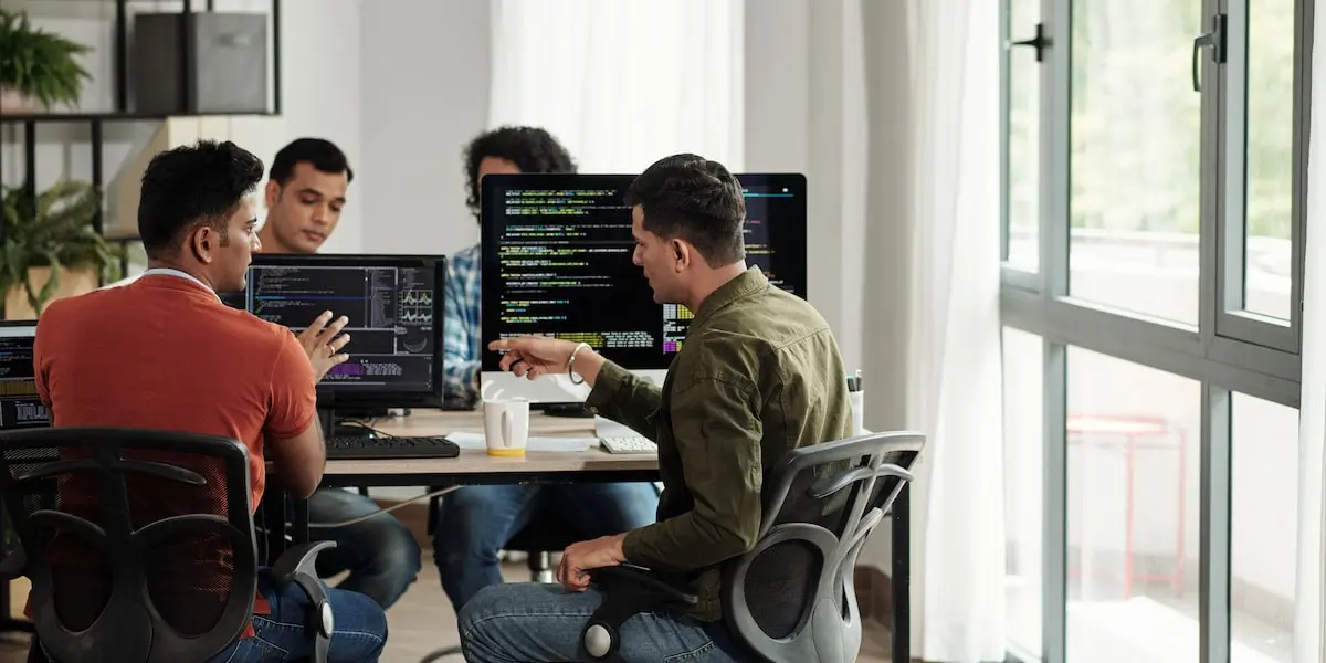 Four cloud engineers sit in an office discussing AWS EC2 at their computers.