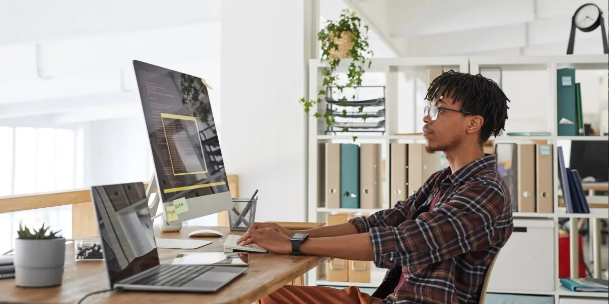 A man sits at a laptop and monitor learning how to become a software engineer.