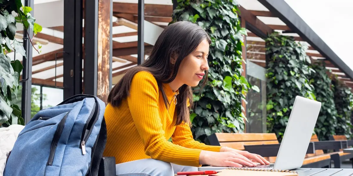 A woman sits outside on a laptop comparing coding vs programming.