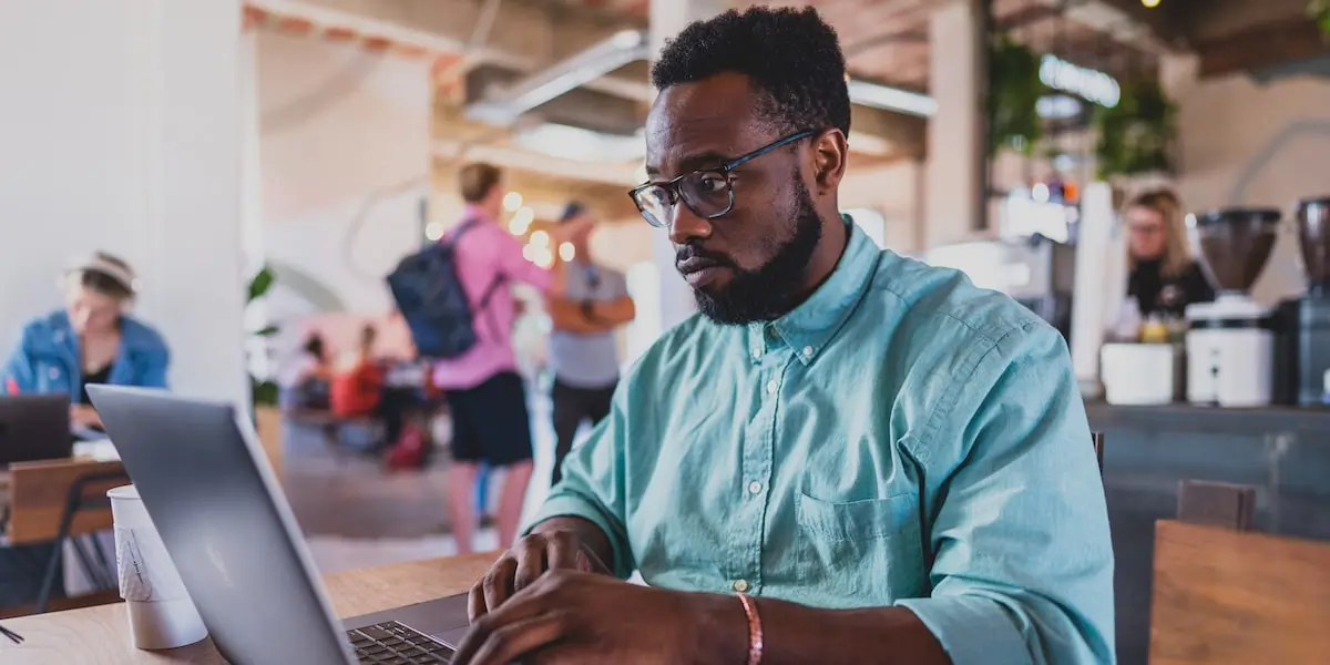 A man sits in a cafe working on his product manager resume on a laptop.