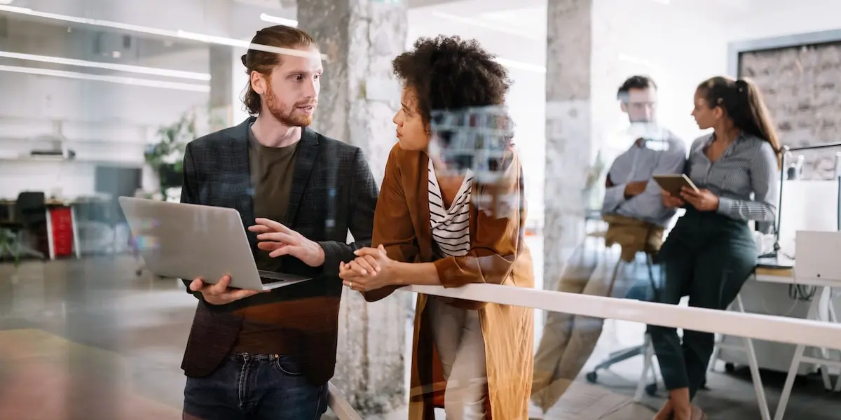 Two PMs at a product management school discuss a project on a laptop.