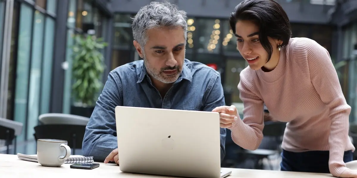 A product manager shows a proof of concept to her colleague on a laptop in an office.