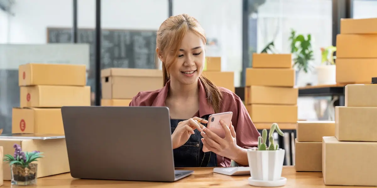 Digital marketer using social media—one of the most popular types of digital marketing—in an office full of stock boxes and a laptop