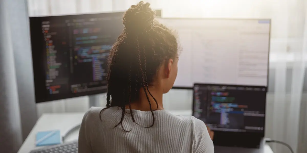 Woman taking a JavaScript bootcamp works on her desktop computer with three screens of JavaScript code.