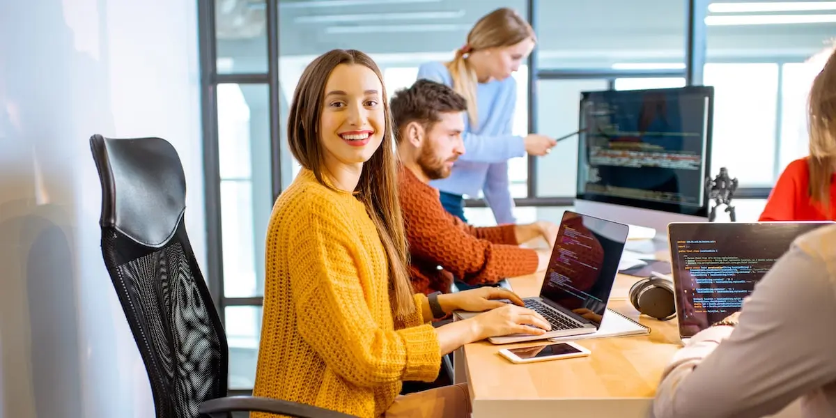 A woman sits in an office carrying out coding jobs with her colleagues at a desk.