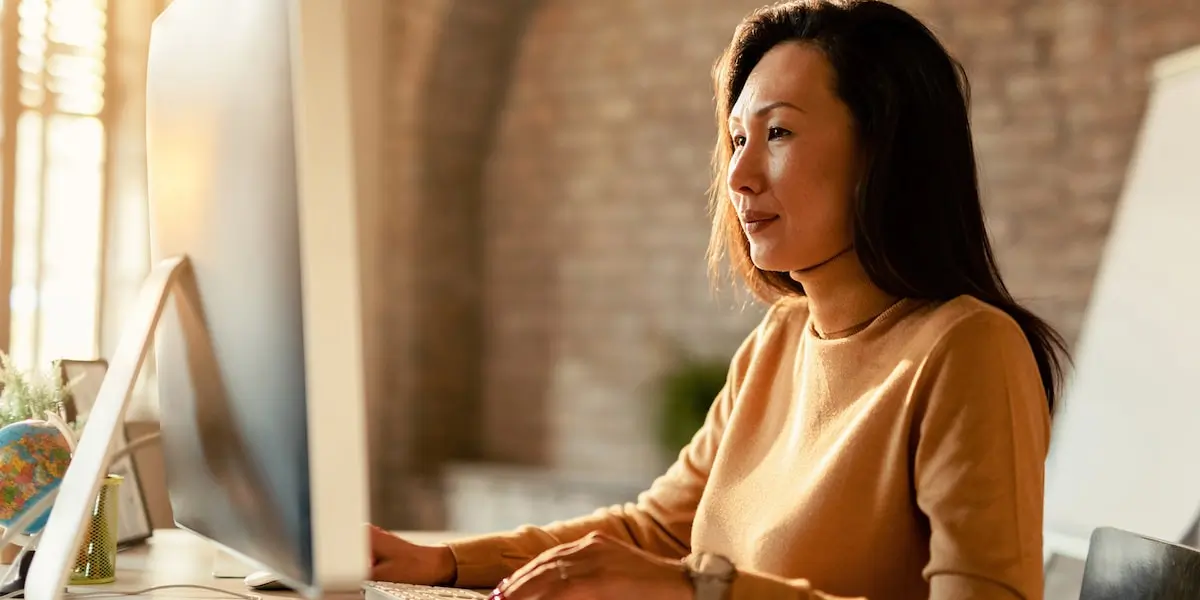 Woman sits in a bright home office at a desktop learning what is web development.