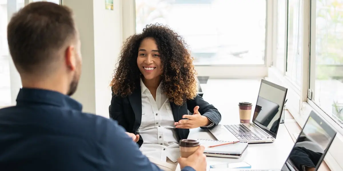 A technical product manager discusses a project with her colleague in an office.