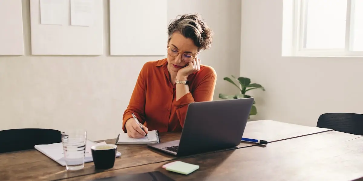 What does a copywriter do? This copywriter writes ideas in her notebook in front of her laptop.