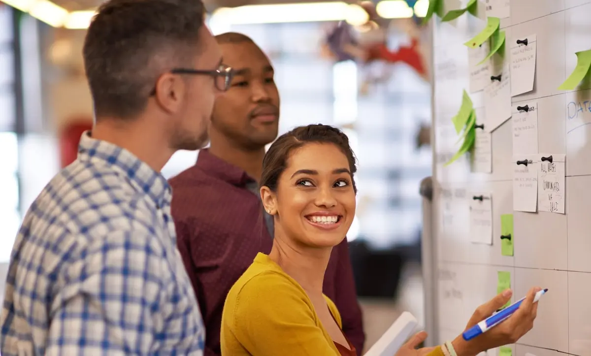 A product manager looks at her colleague while writing on a Scrumban board in an office.