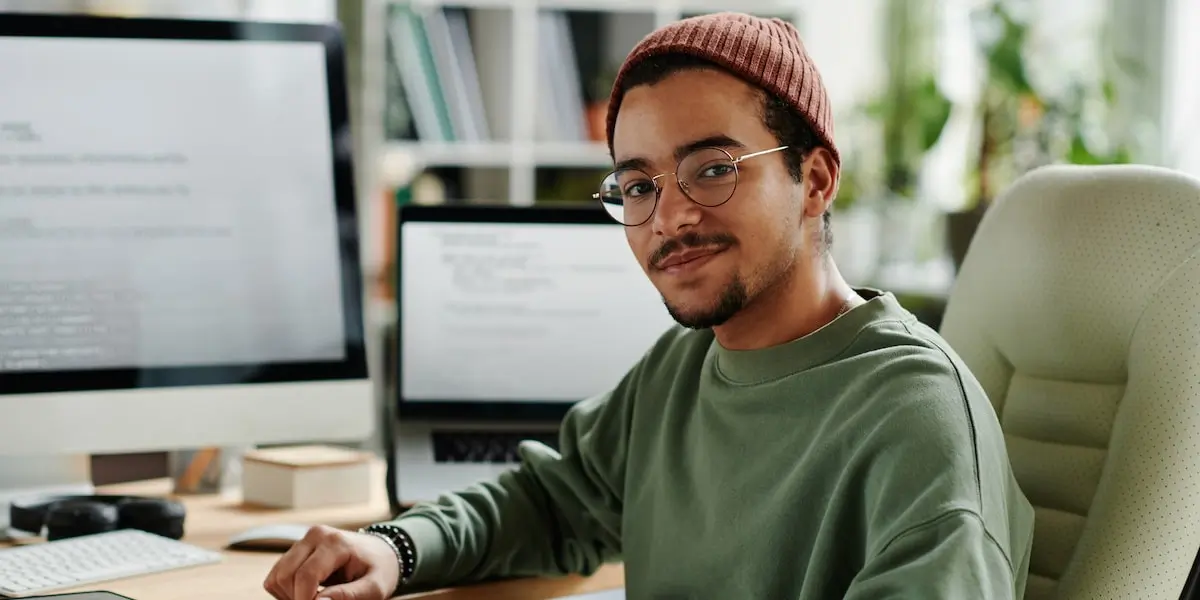 A man working an entry-level programming job sits at his desk looking at the camera.