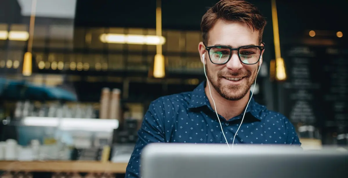 An AI product manager works on his laptop with headphones in a cafe.