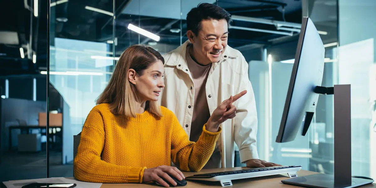 Two ux designers at a computer, one standing and one sitting pointing at the screen, using ai in ux design