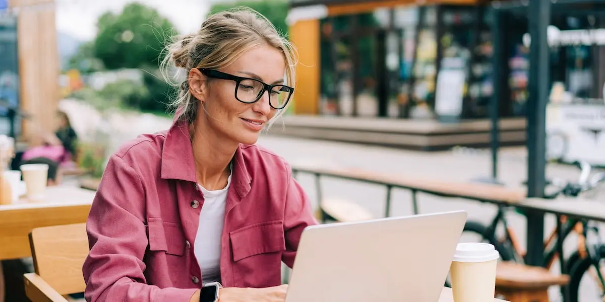 A young blonde businesswoman sits outside at her laptop using chatgpt to write her resume