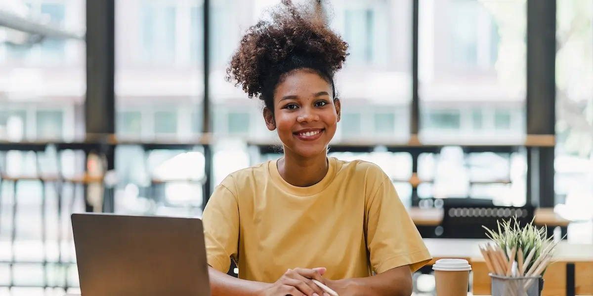 Young woman at her laptop studying an online AI course smiles at the camera