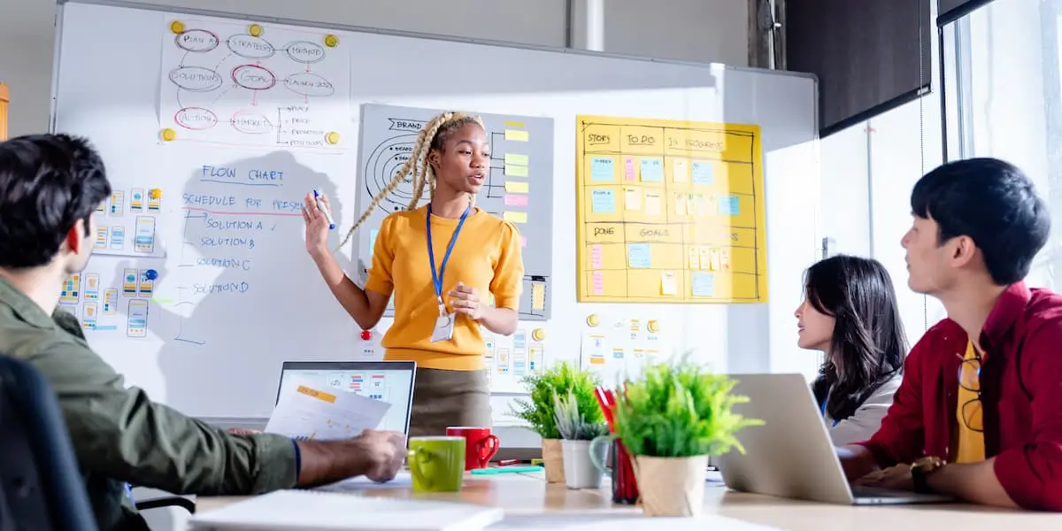 A product operations manager presents at a whiteboard to her team.