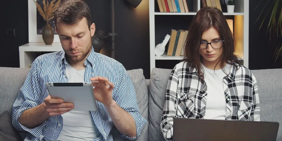 A couple sit at a couch using Llama and ChatGPT on their tablet and laptop