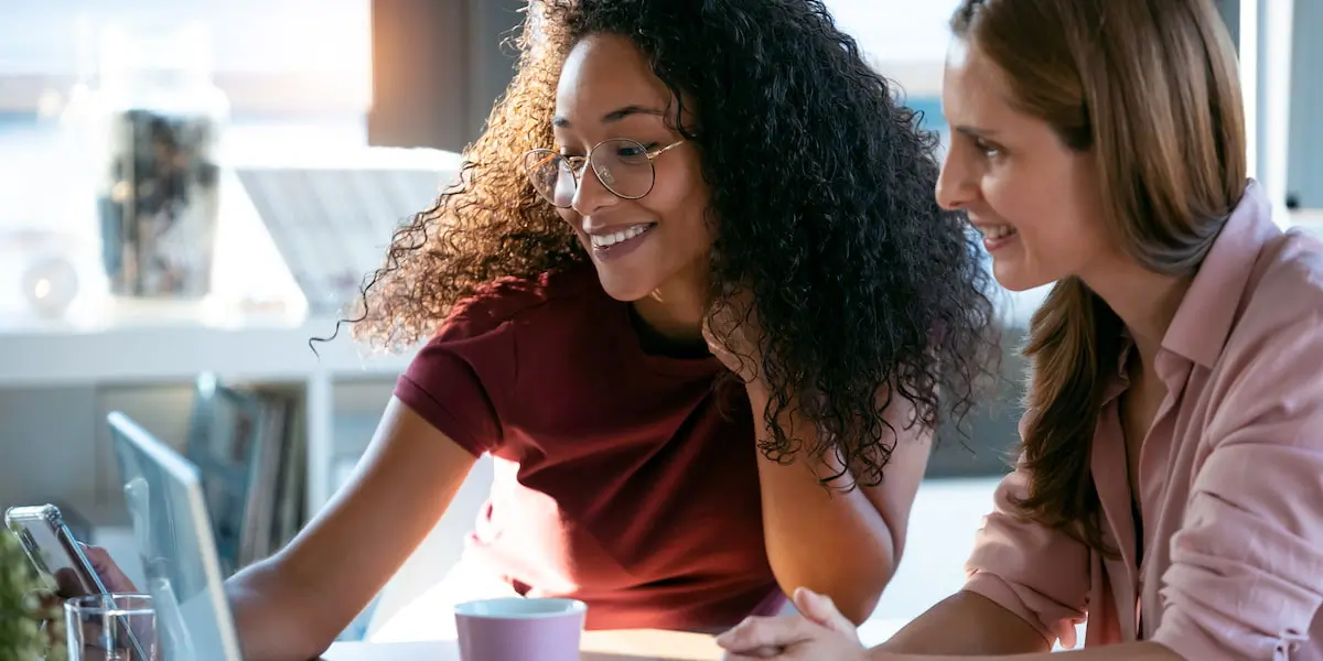 A young female UX manager instructs her colleague on a UX project while both sit at a desk.