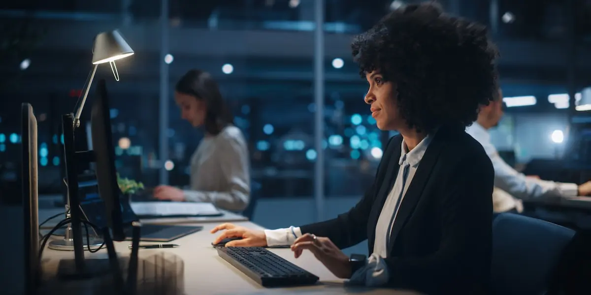 An email marketing specialist works at her desktop computer at night