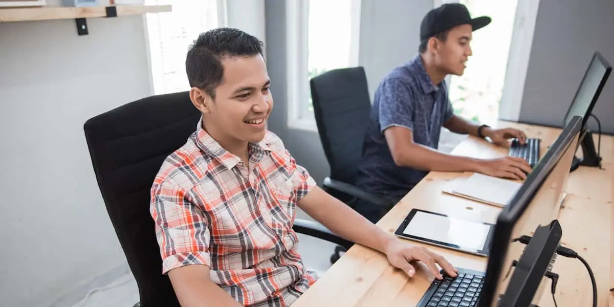 Two men sitting beside each other pair programming at their computers.