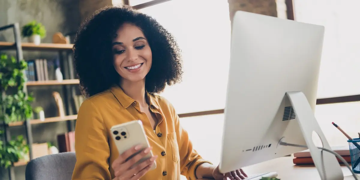 A young female aspiring UX designer researches UX bootcamp Reddit advice on her phone and laptop